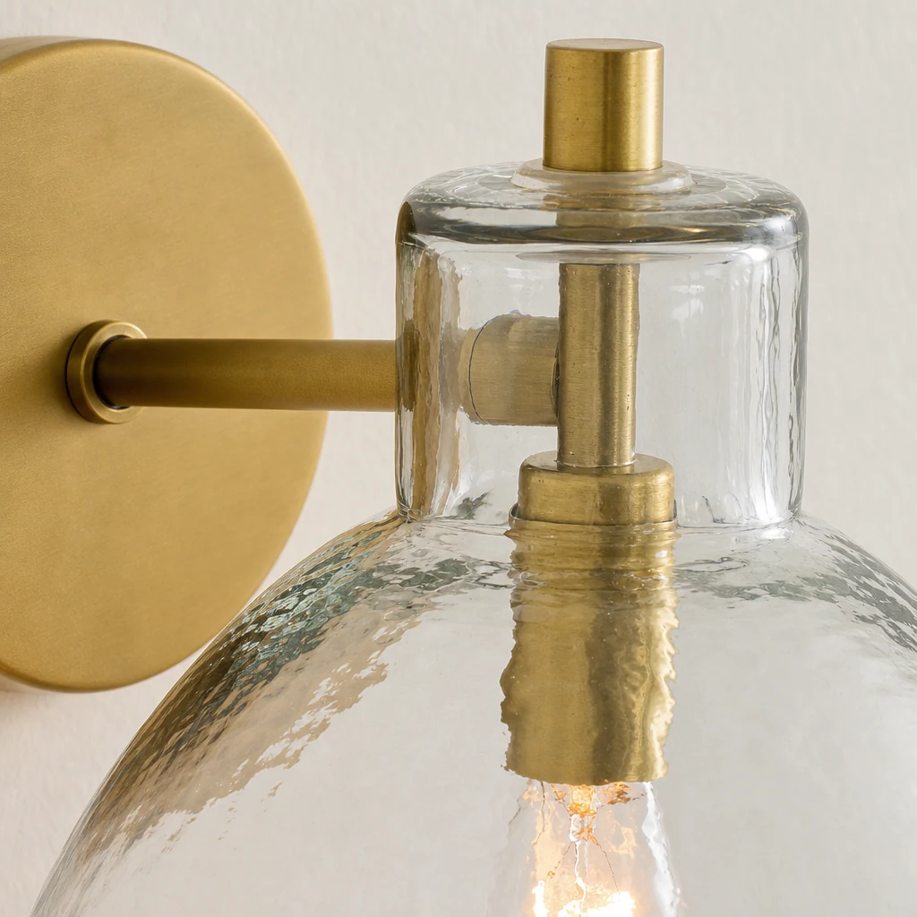 Detailaufnahme der Wandleuchte Glavira: Messingoberfläche und klarer Glasschirm