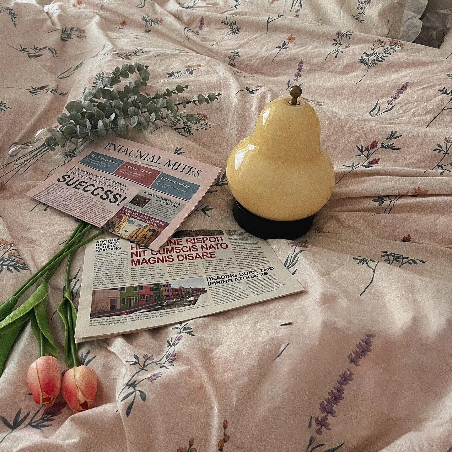 Lampa gruszkowa ustawiona na pościeli z książkami i kwiatami