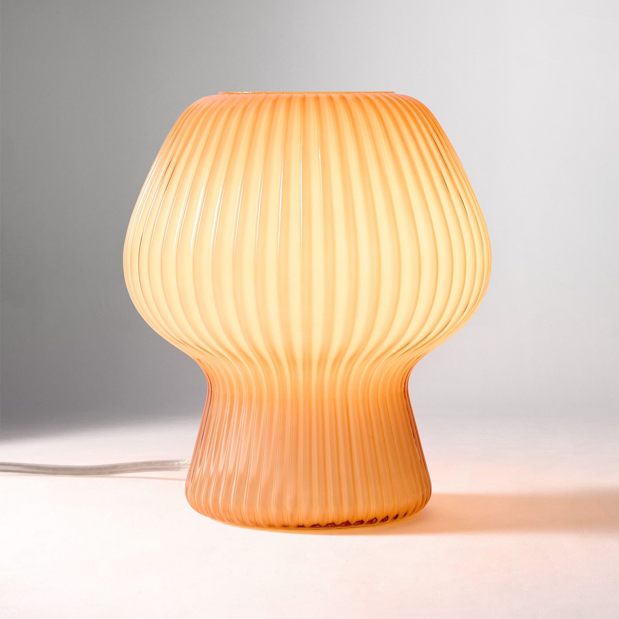 Bärnstensfärgad ribbad glasbordslampa som lyser på enfärgad bakgrund