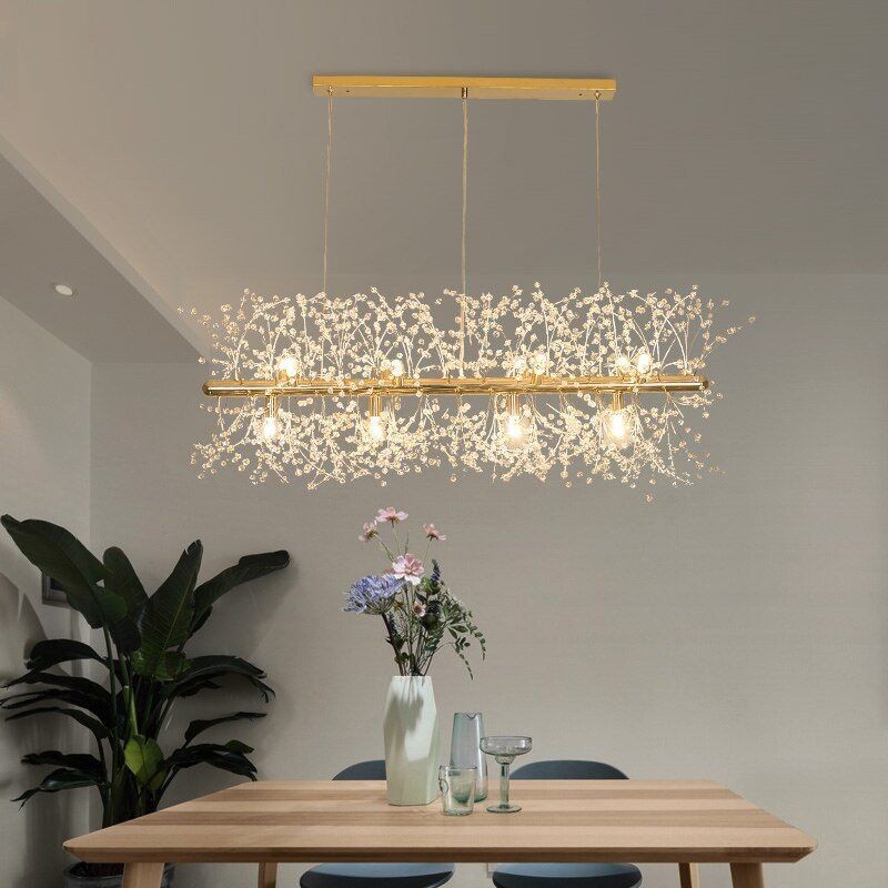 Escena minimalista de comedor con lámpara de araña de cristal sobre una mesa y plantas.