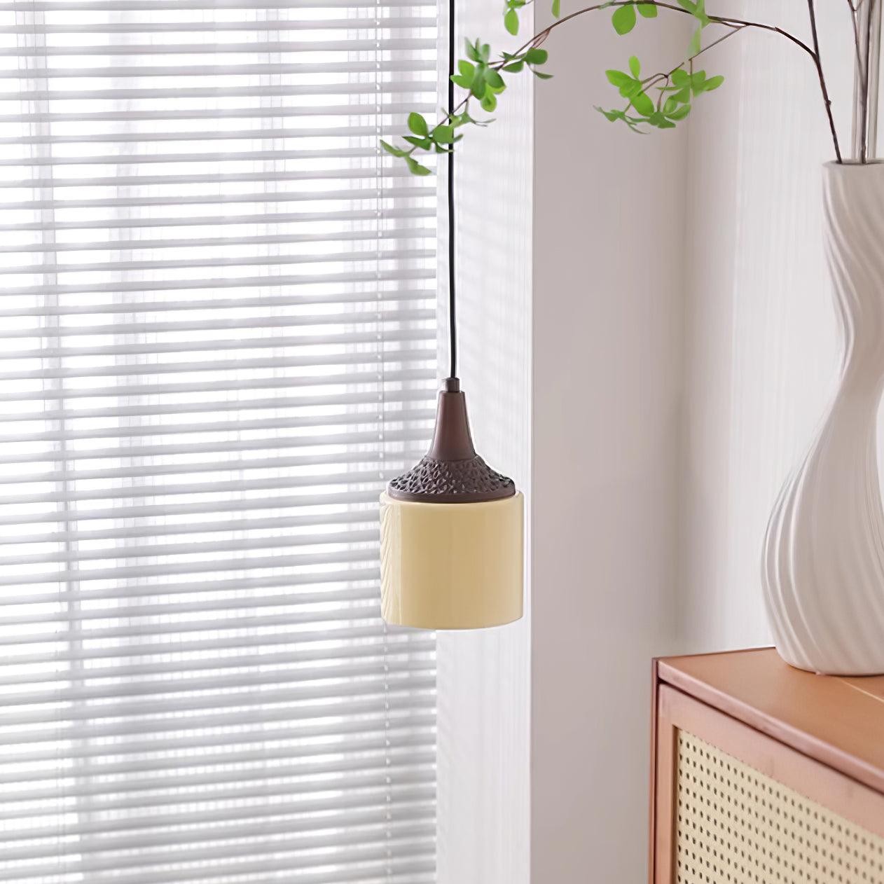Cylindryczna lampa wisząca oświetlana w pobliżu okna i szafki