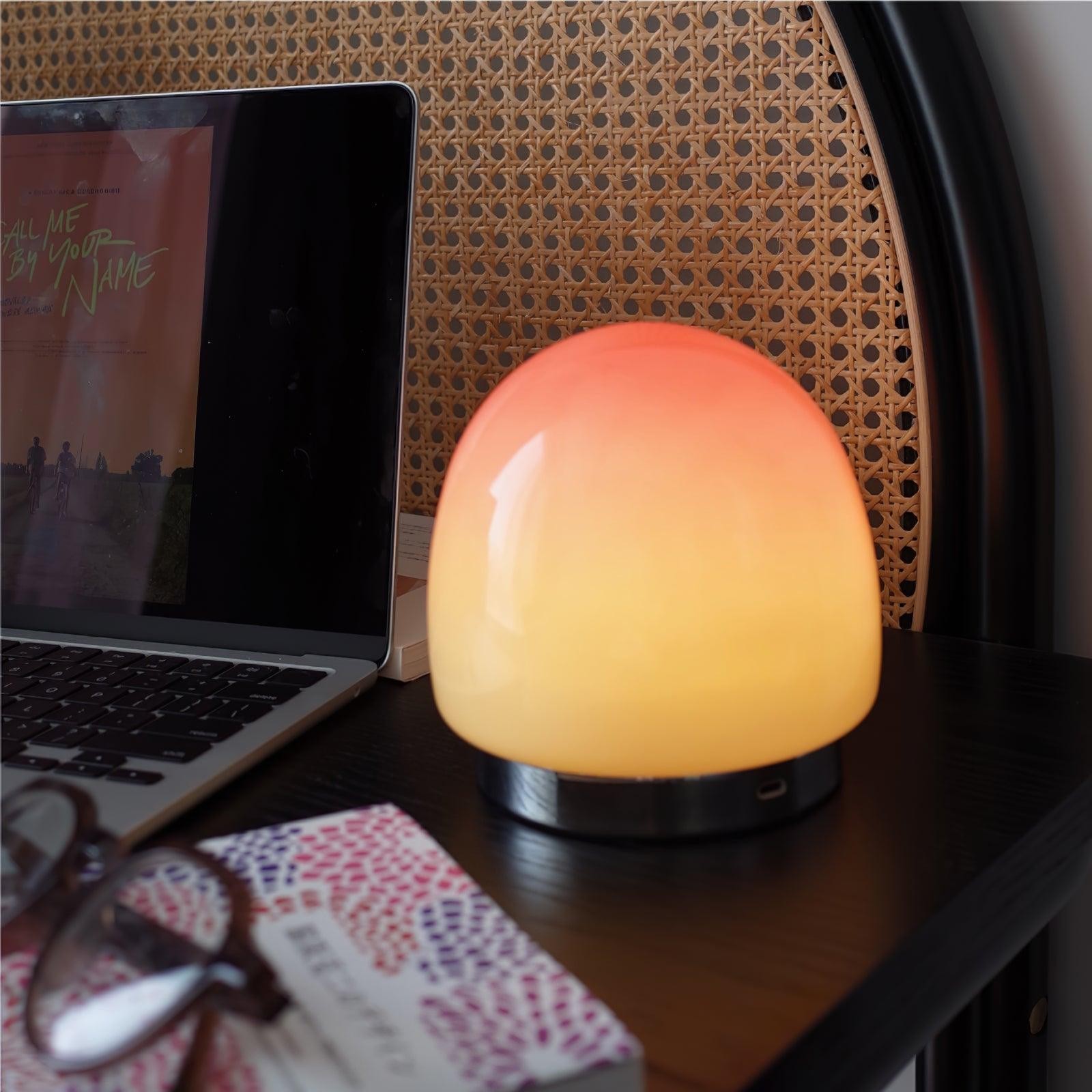 Brzoskwiniowa lampa stołowa świecąca obok laptopa