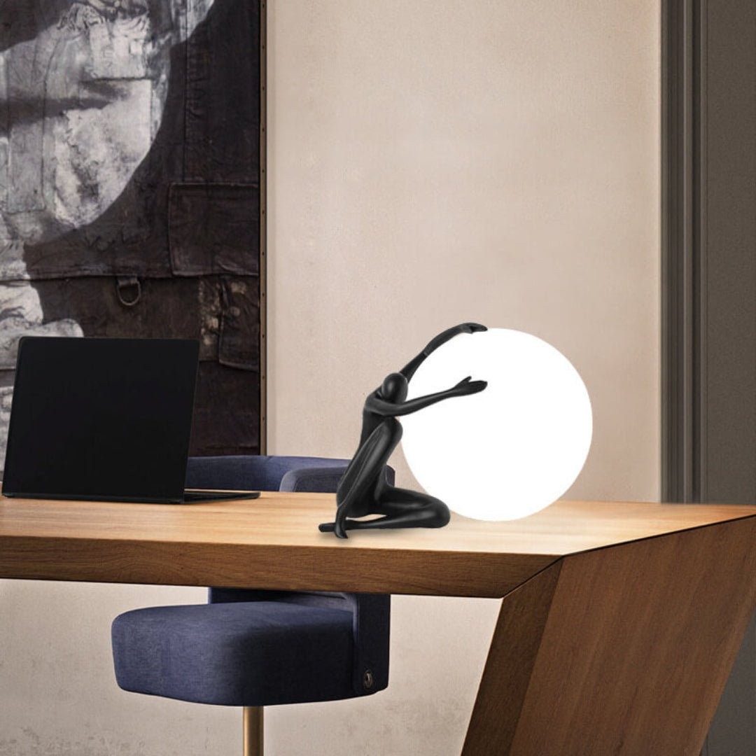 Humanoid ball som holder bordlampe M585 på et skrivebord i et rom