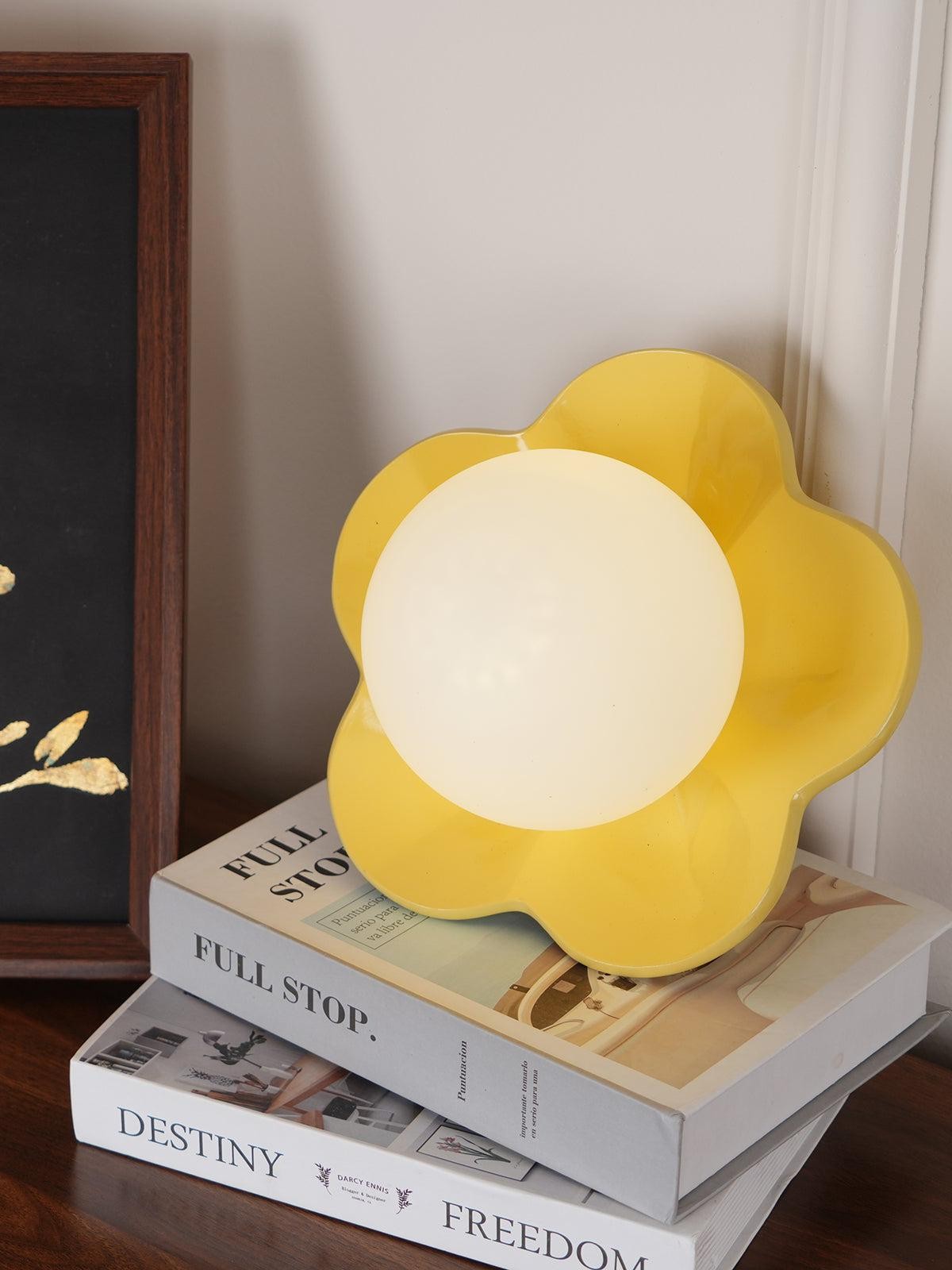 Żółta lampa La Fleur wystawiona na książkach z dekoracjami