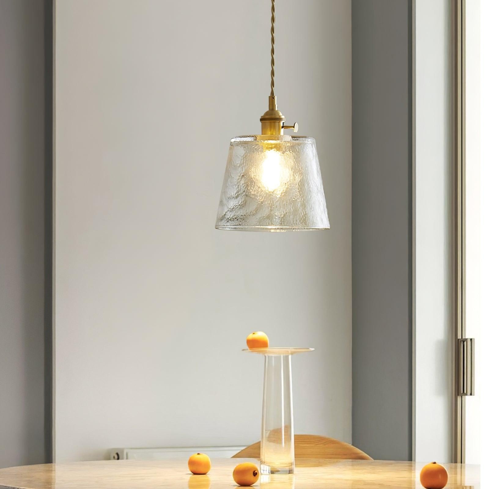 Pendellampe i klart glass over en liten bordplate med frukt