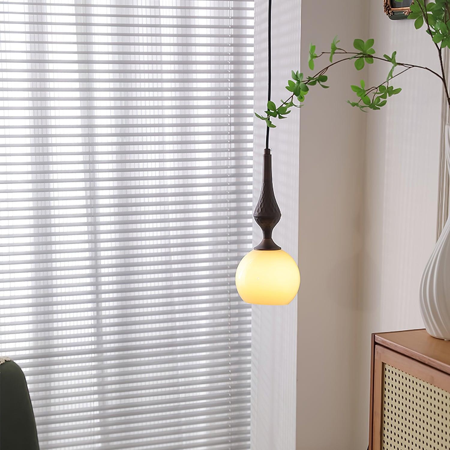Mała lampa wisząca w kształcie kuli, zapalana obok żaluzji okiennych