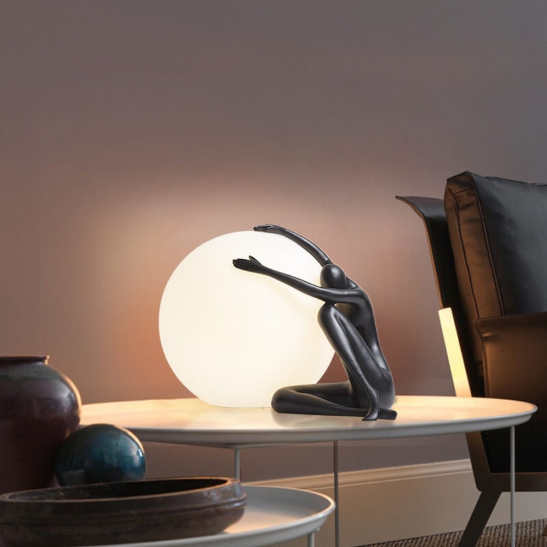 Humanoid ball som holder bordlampe M585 på et bord i et møblert rom