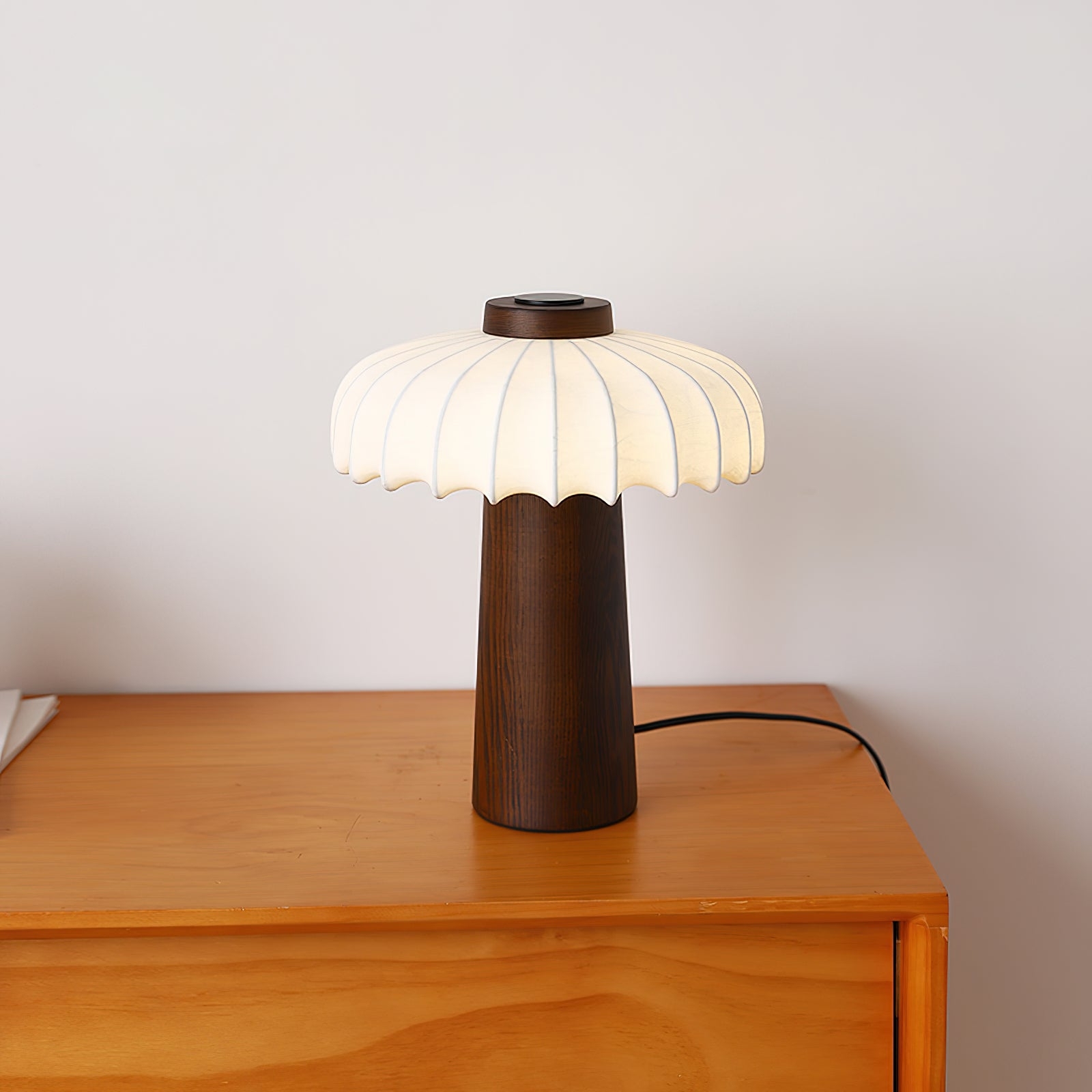 Lampa stołowa Juego z ciemnego drewna zapalona na szafce