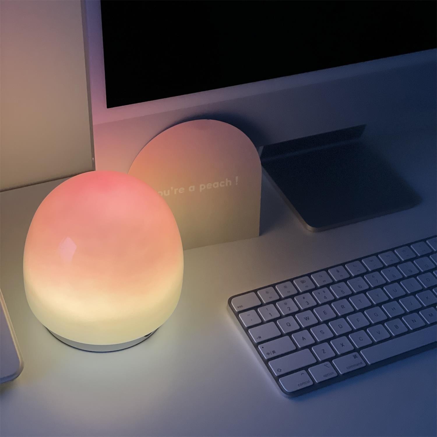 Brzoskwiniowa lampa stołowa w pobliżu monitora i klawiatury