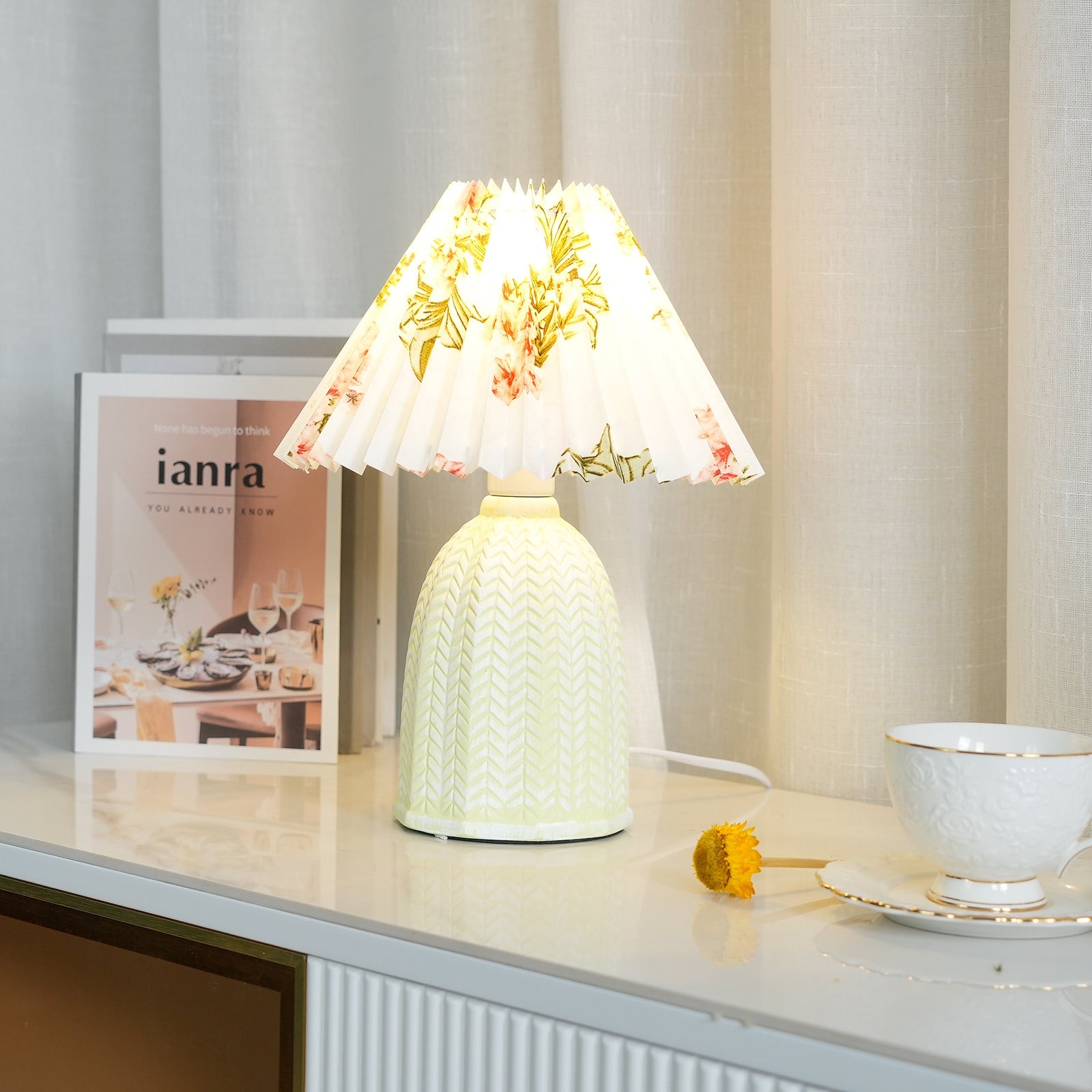 Vintage plisowana lampa stołowa eksponowana na szafce z książką i filiżanką