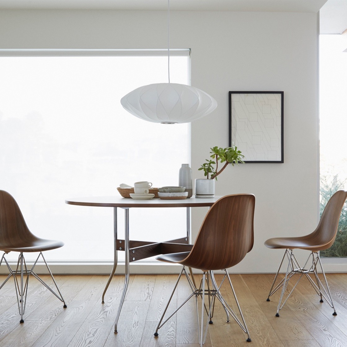 Lámpara colgante blanca con forma de platillo sobre una mesa de comedor minimalista.