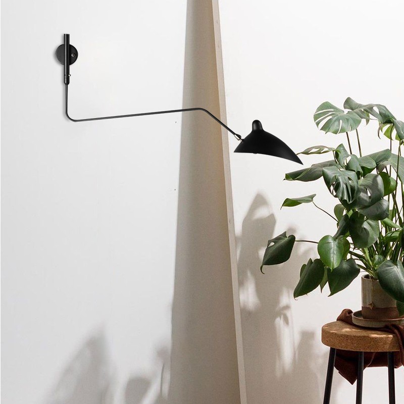 Svart andenebb-vegglampe montert i nærheten av en plante og et bord