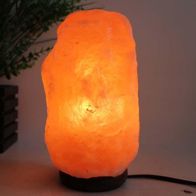 Lámpara de mesa central de sal del Himalaya con luz brillante y fondo vegetal.