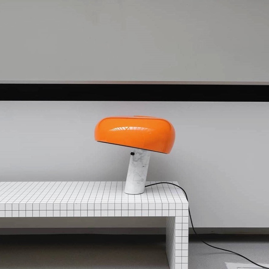 Lámpara de mesa curva de mármol naranja sobre un banco minimalista de azulejos.