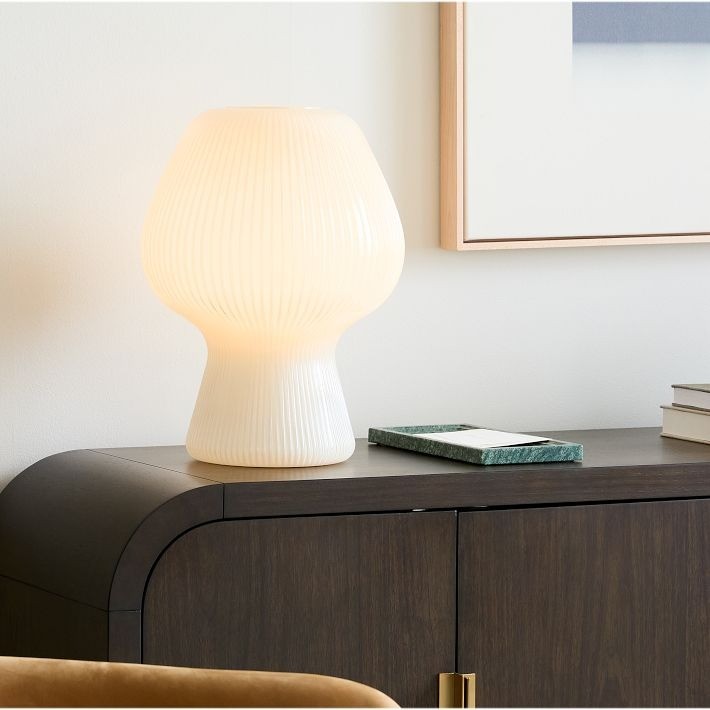 Ribbad glasbordslampa på ett mörkt skåp med inramad väggkonst