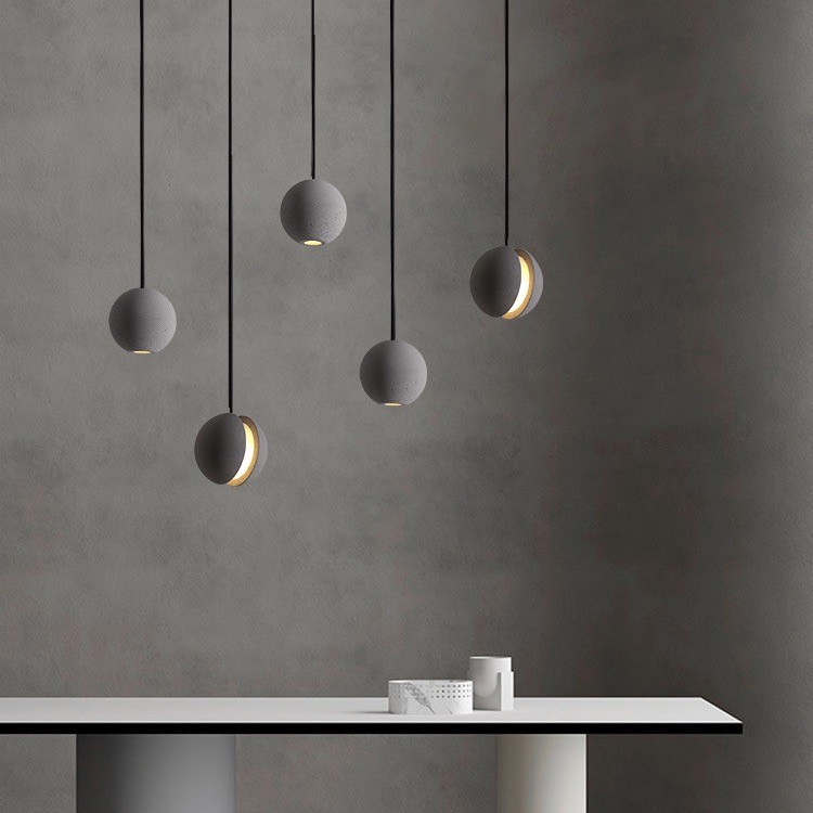 Flere pendellamper over et minimalistisk bord og en teksturert vegg