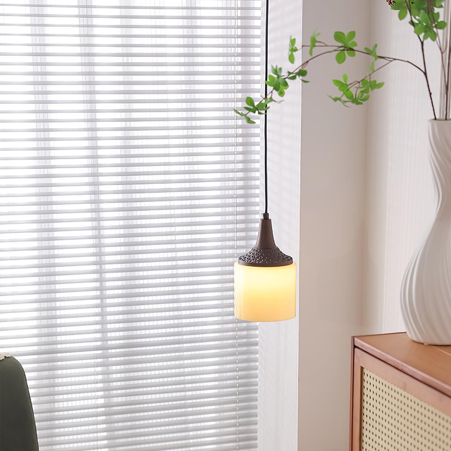 Cylindryczna kremowa lampa wisząca oświetlana w pomieszczeniu