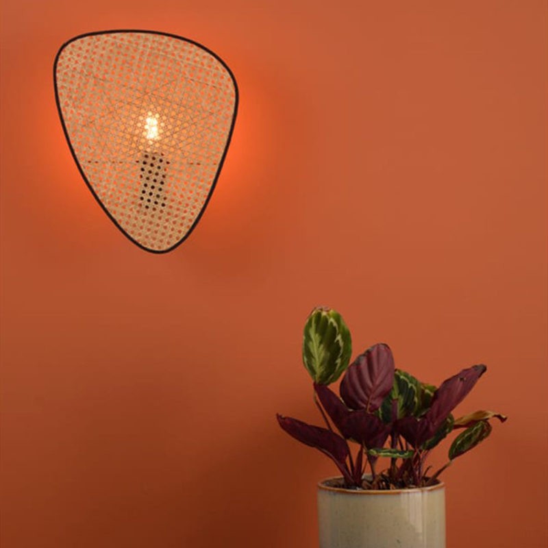 Rattan-Wandleuchte an einer warmfarbigen Wand mit Pflanzendekoration
