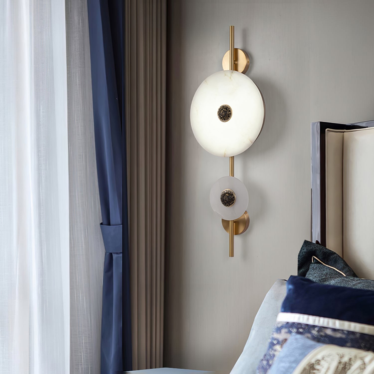 Double-disc wall lamp beside curtains and bedding