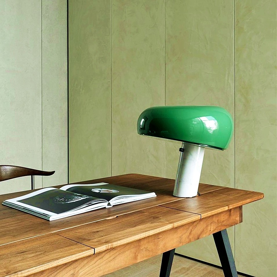 Lámpara de mesa curva de mármol verde sobre un escritorio de madera con libros.