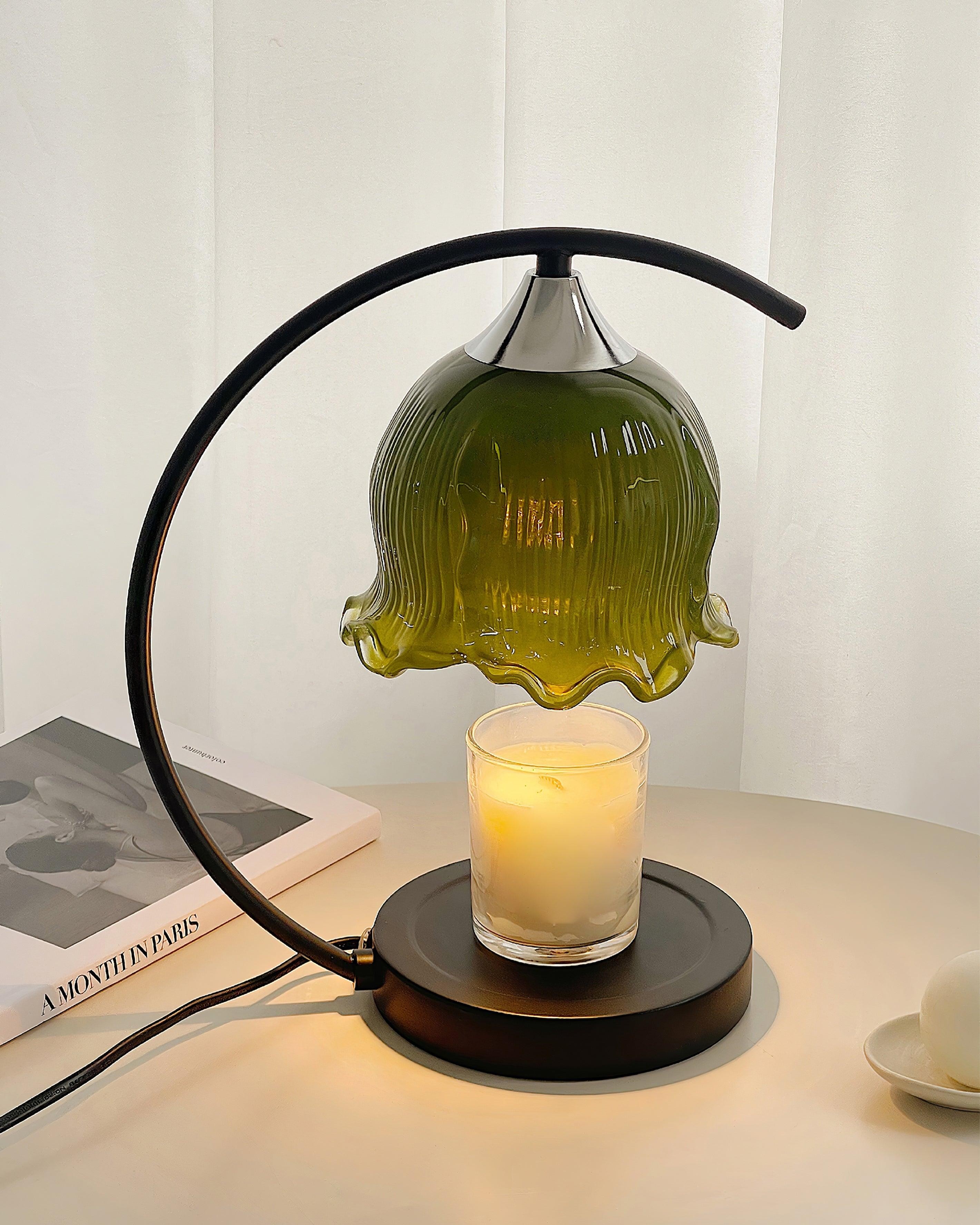 Lampa podgrzewająca świecę w zielonym odcieniu obok książki i filiżanki