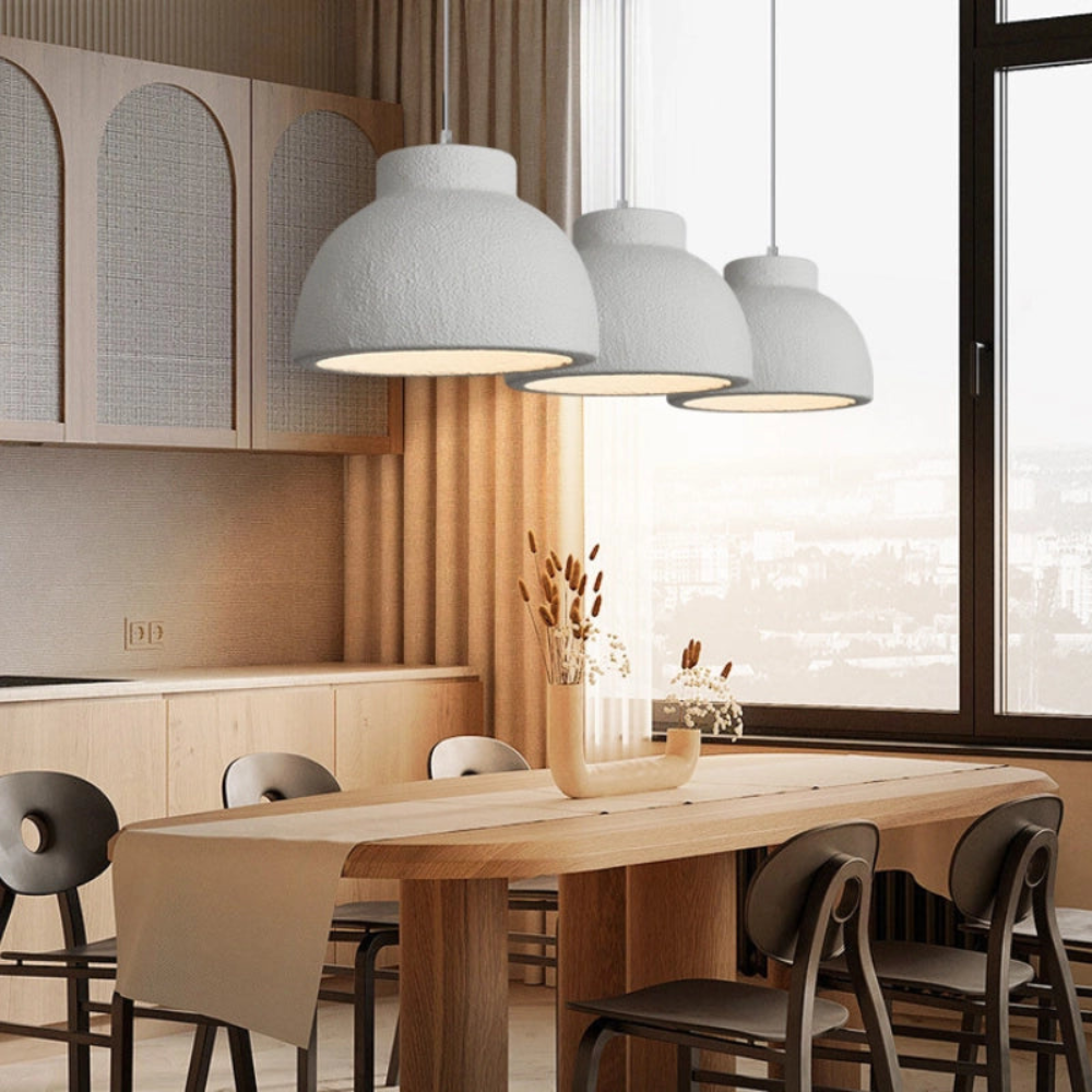 Tres lámparas colgantes blancas sobre una mesa de comedor luminosa.