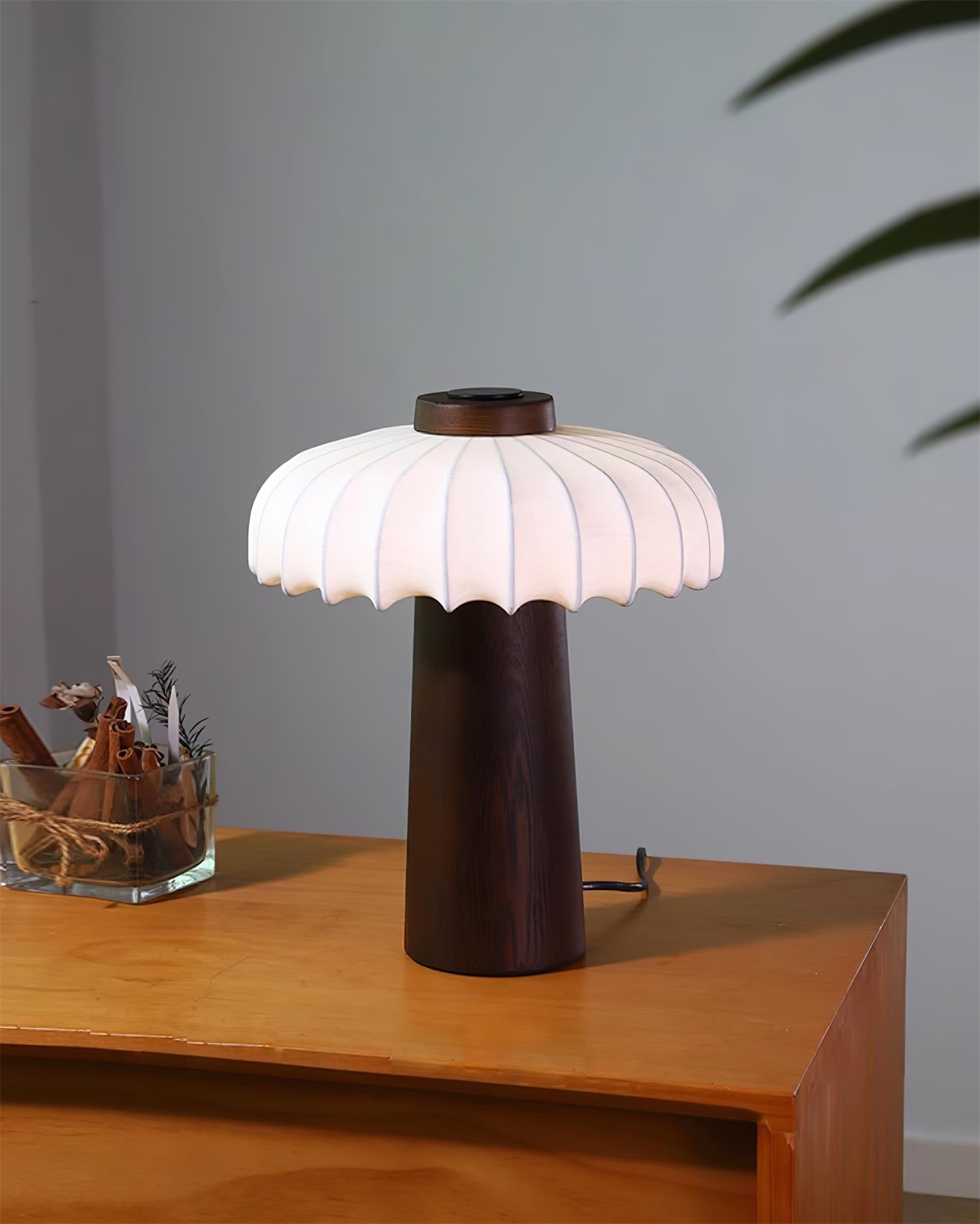 Lampa stołowa Juego z ciemnego drewna rozświetlona nastrojową sceną na blacie