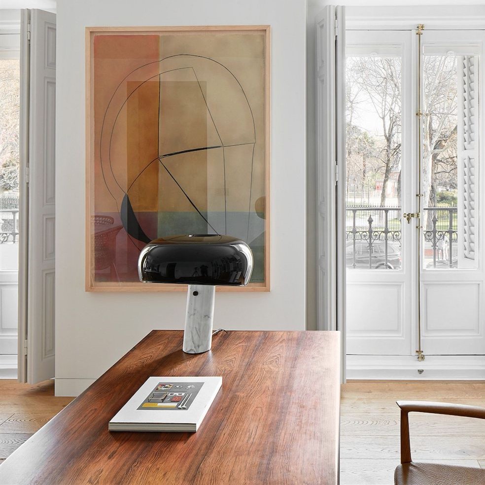 Lámpara de mesa curva de mármol sobre una mesa de madera en una habitación luminosa.