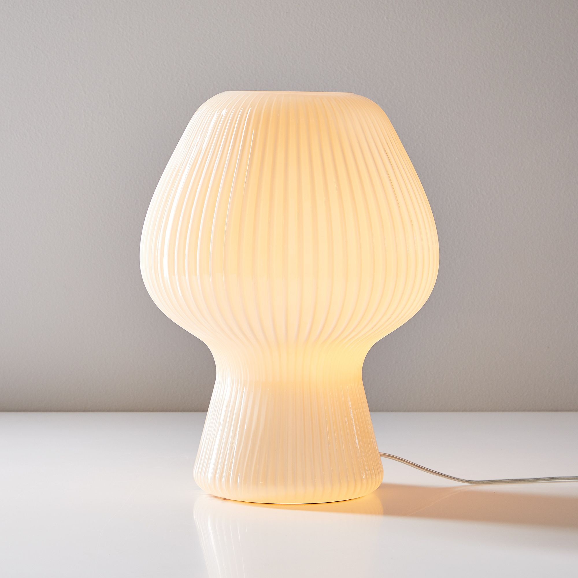 Bordlampa i champagnefärgat räfflat glas som lyser med synlig, klar sladd