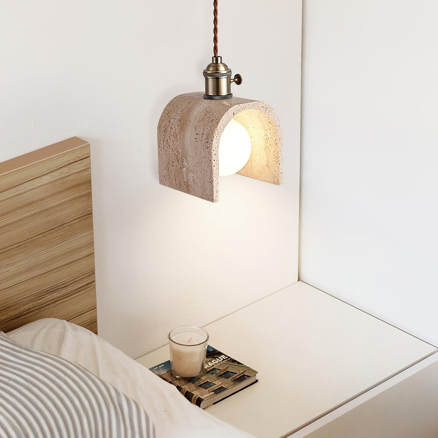 Łukowata lampa wisząca z trawertynu oświetlana nad szafką nocną w sypialni