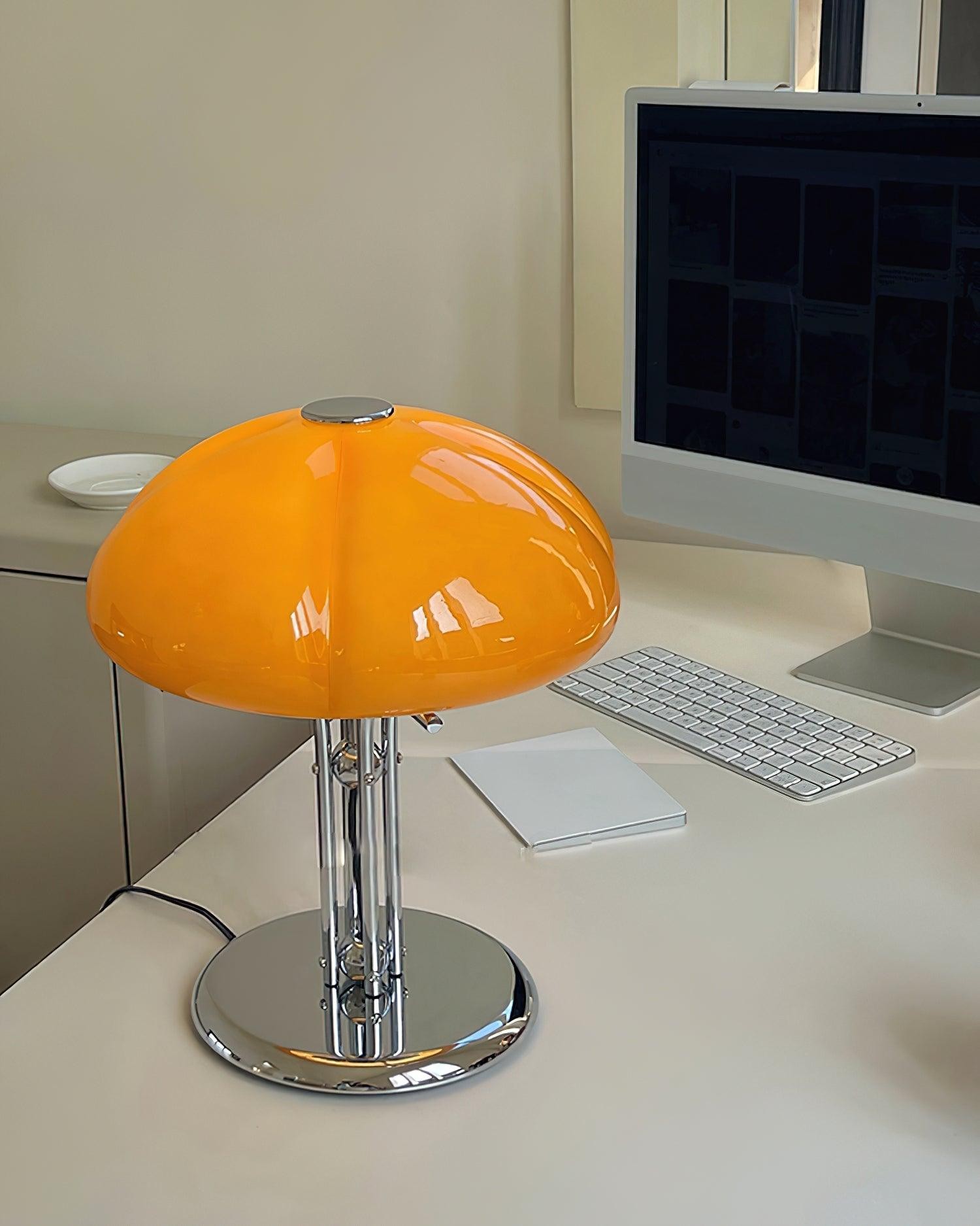 Pomarańczowa szklana lampa na biurku obok monitora i klawiatury
