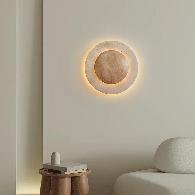 Aplique de pared redondo de madera de travertino D880 iluminado sobre una mesa auxiliar y un sofá.