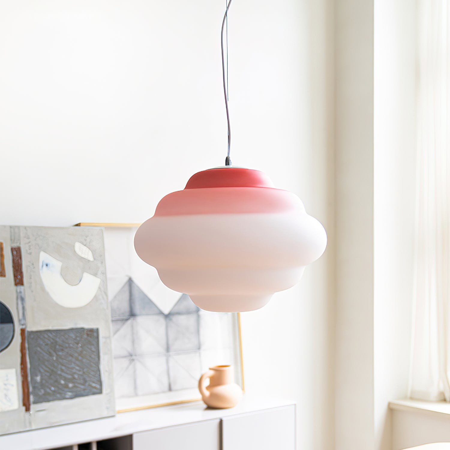 Rød gradient pendellampe ved et lyst vindu og kunstverk