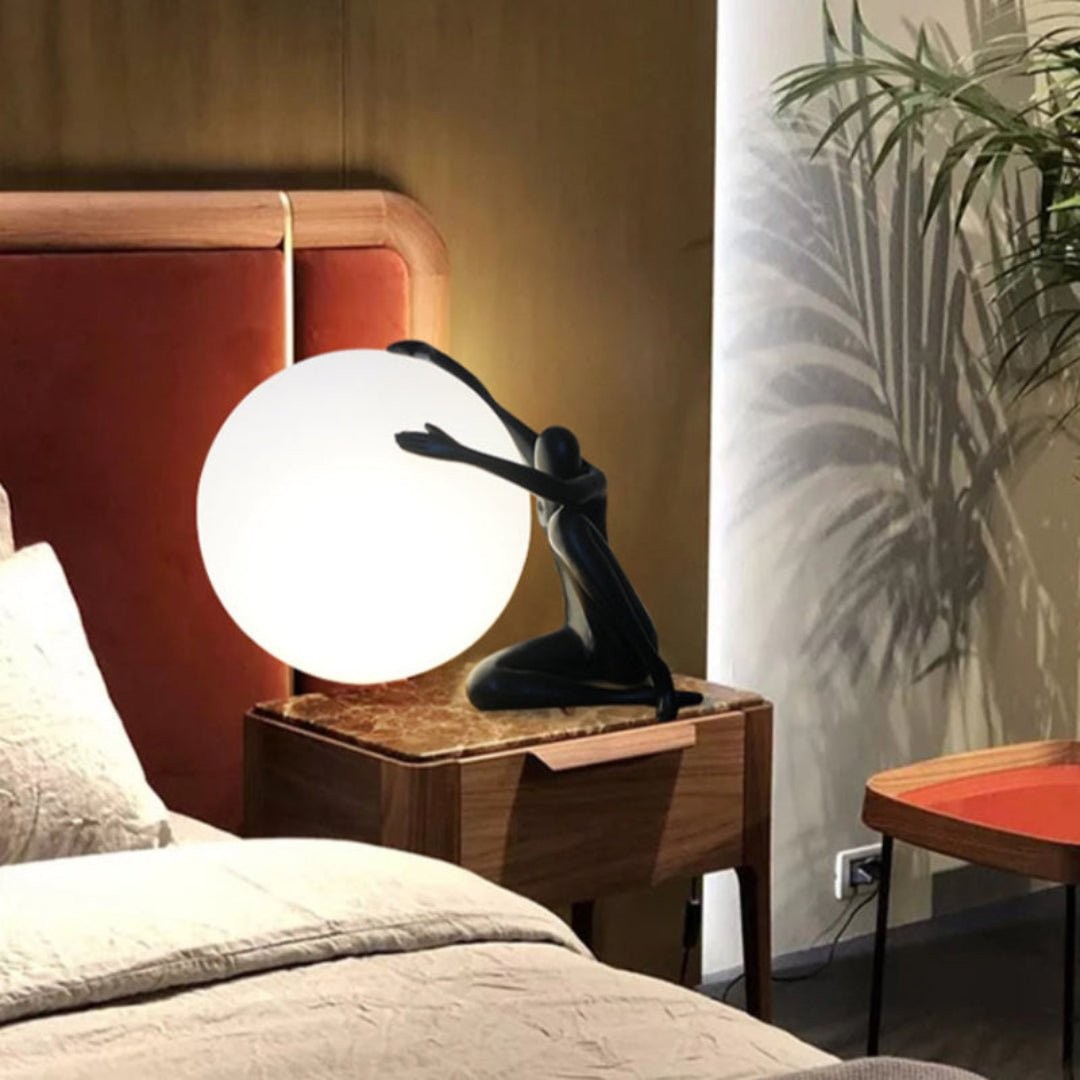 Svart humanoid ball som holder bordlampe M585 på et nattbord på soverommet