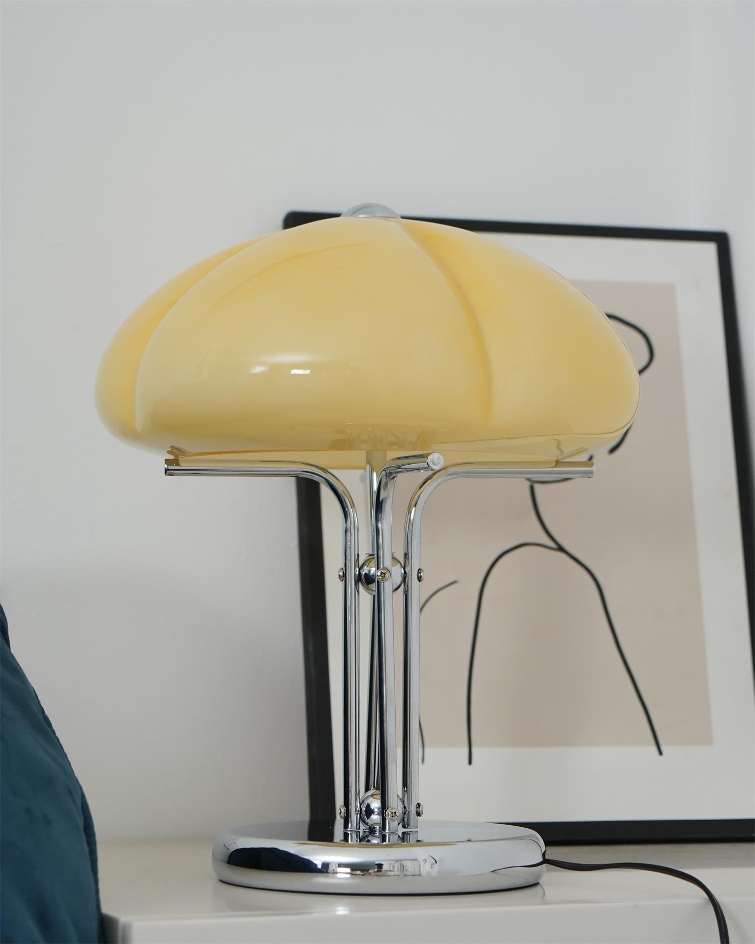 Kremowo-żółta szklana lampa stojąca na stoliku nocnym z grafiką ścienną
