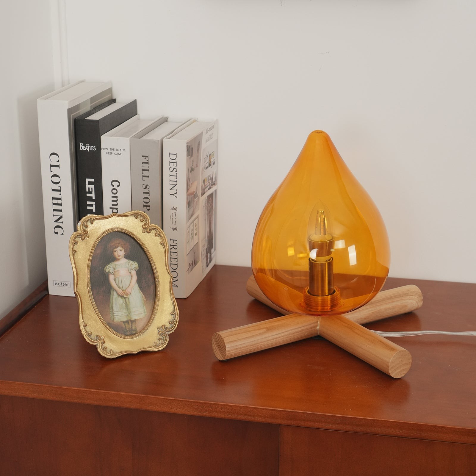 Lampa płomieniowa umieszczona obok książek i oprawionego obrazu