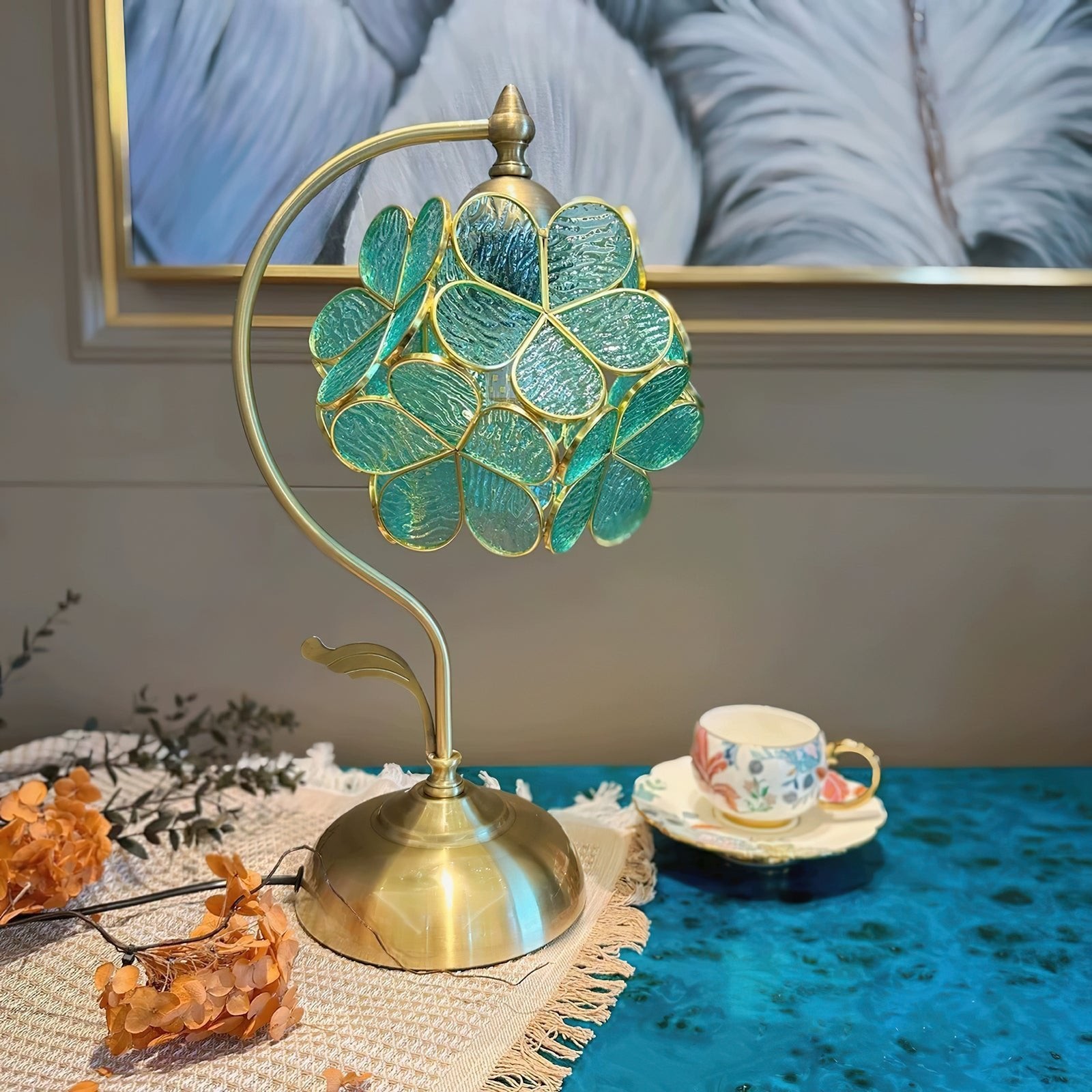Grønn glasslampe med kronblader ved siden av en kopp og dekor