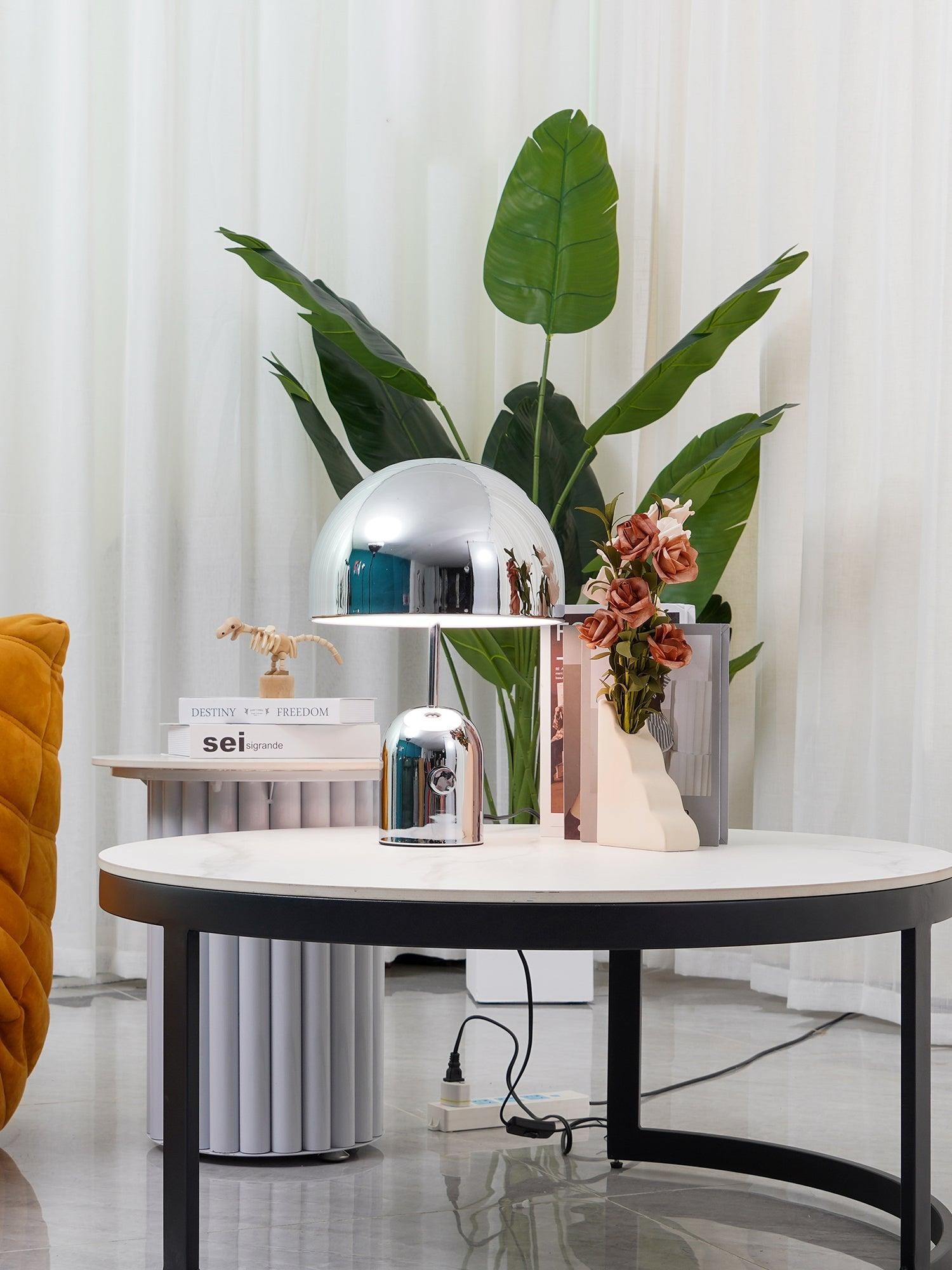 Lámpara de mesa con forma de campana cromada en una habitación luminosa.